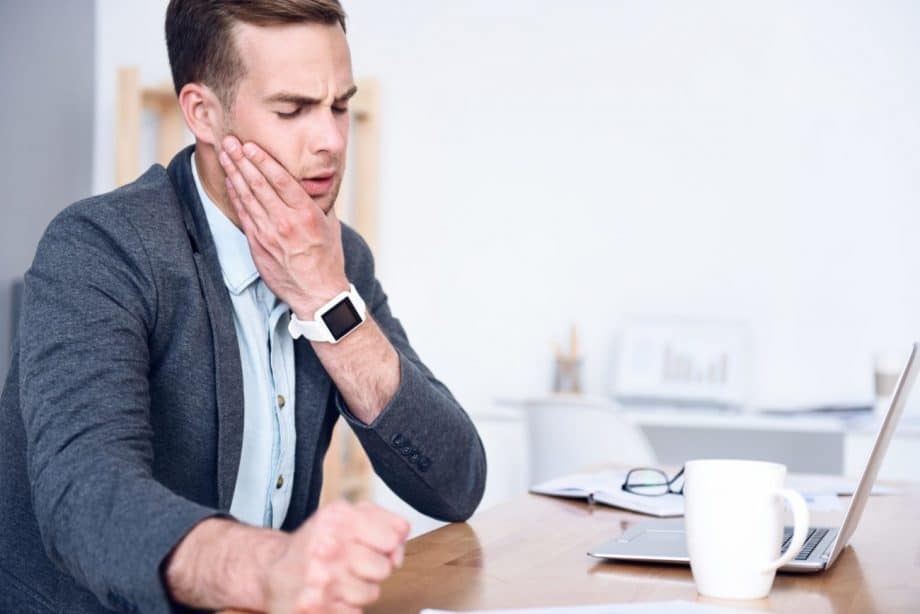 man sitting at desk holding jaw in pain