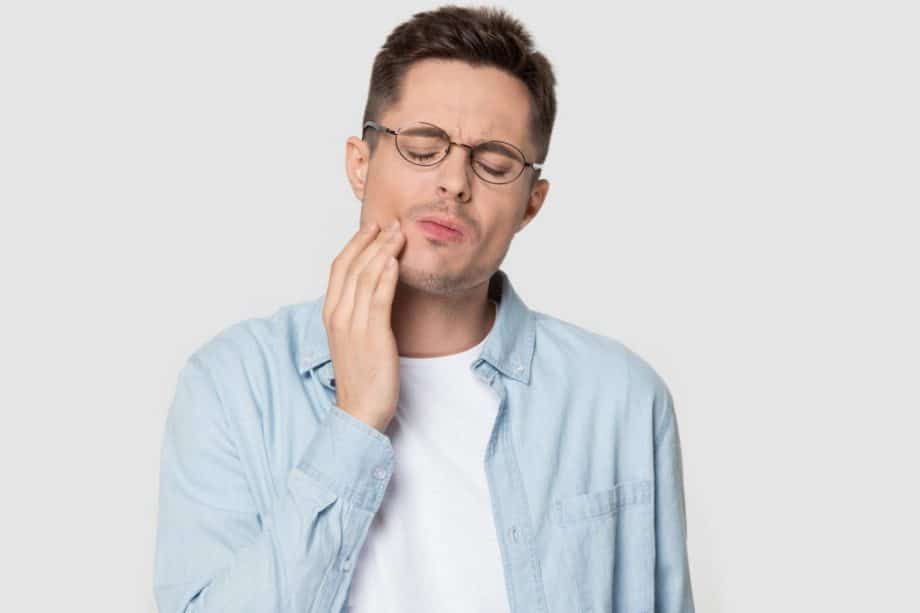 young man in glasses holding jaw in pain