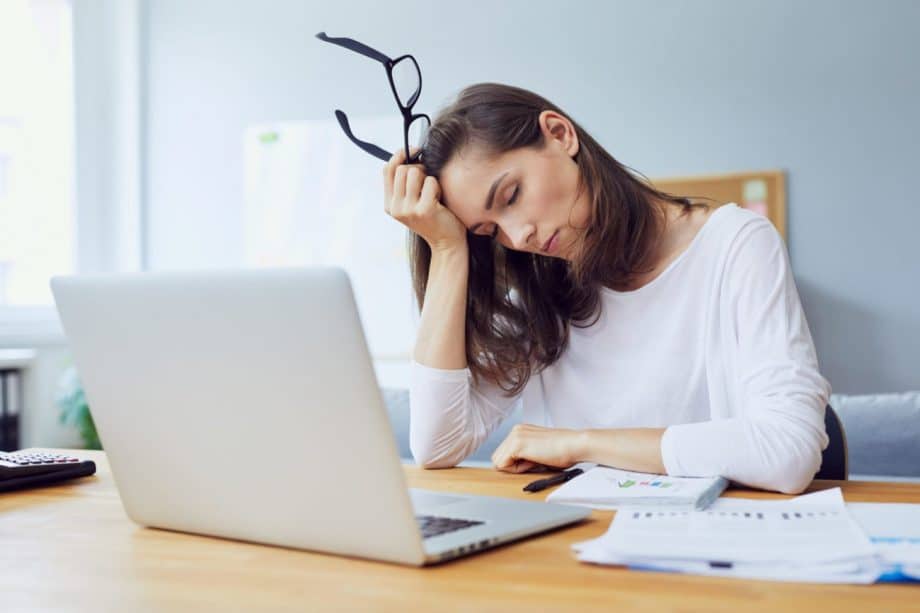 woman sitting in front of laptop with head leaning on hand, eyes closed