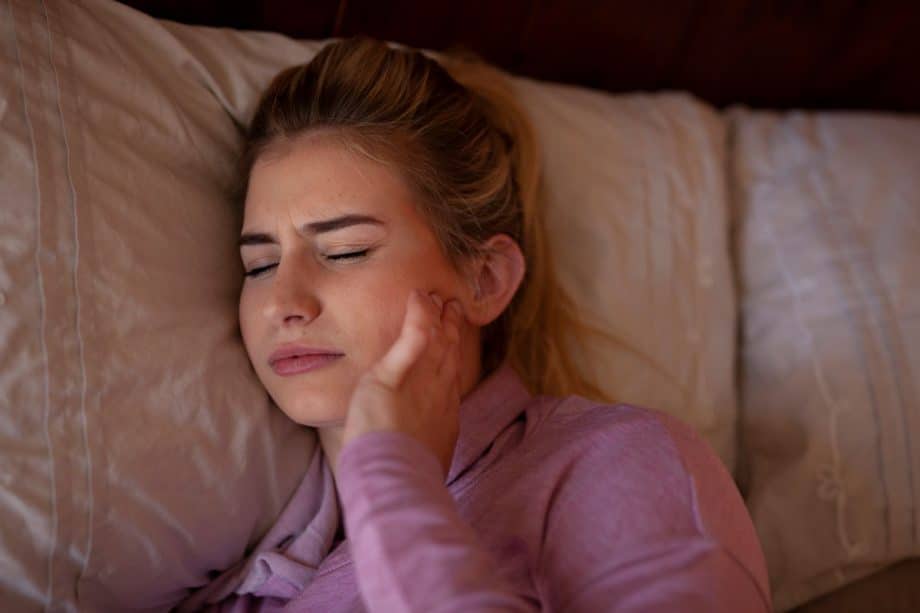 woman laying in bed holding jaw in pain