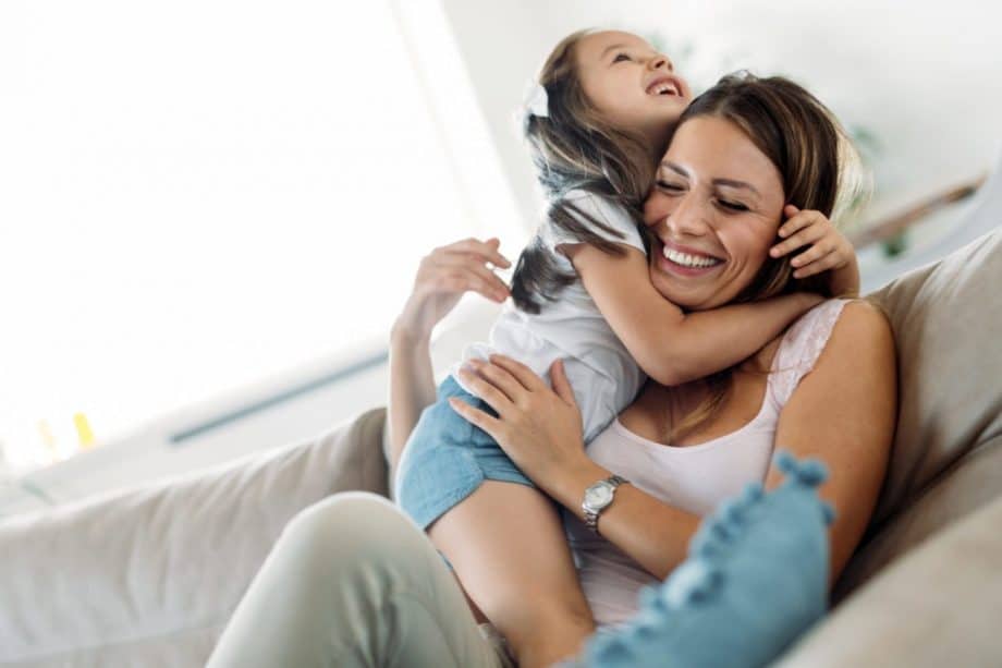 young girl and mother sitting on couch, hugging and smiling