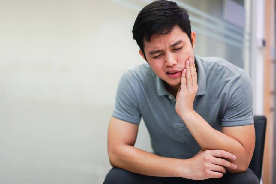 young man sitting in chair holding jaw in pain