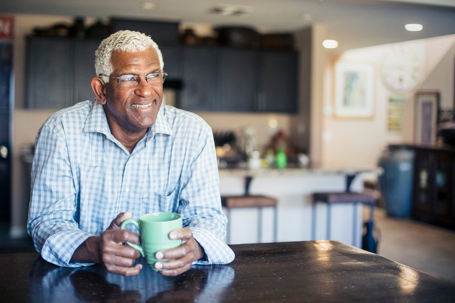 senior man sitting at table with cup of coffee, smiling