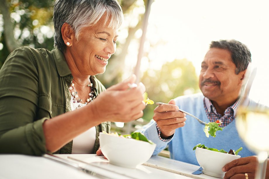 man and woman sitting outside at a table eat salads